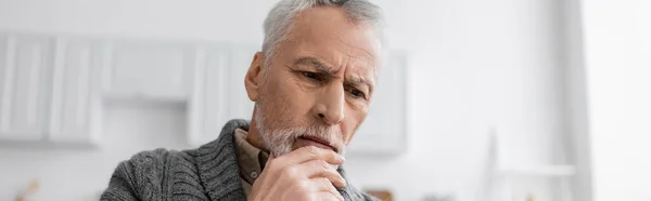 Pensive senior man with alzheimer disease holding hand near chin while thinking at home, banner — Stock Photo