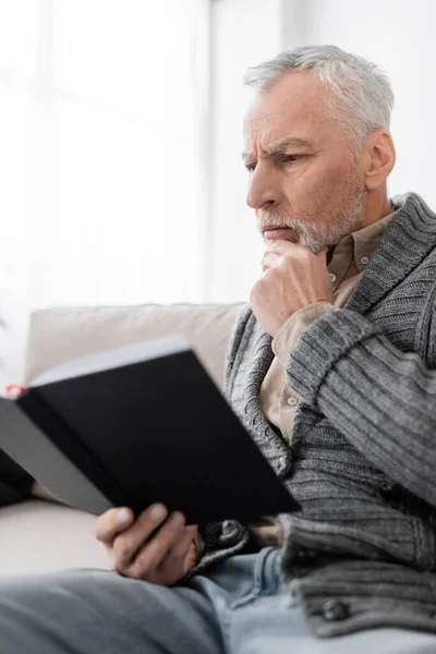 Senior man with alzheimer syndrome touching chin while sitting with notebook at home — Stock Photo