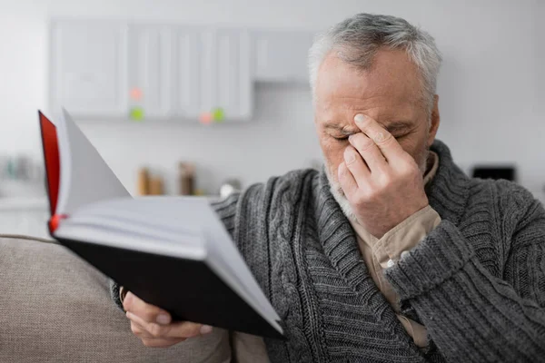 Depressed man with alzheimer syndrome sitting with closed eyes and blurred notebook at home — Stock Photo