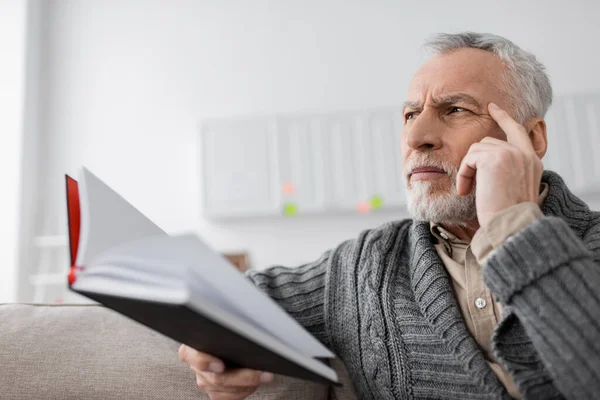 Tense man with alzheimer syndrome touching head and looking away while holding blurred notebook — Photo de stock