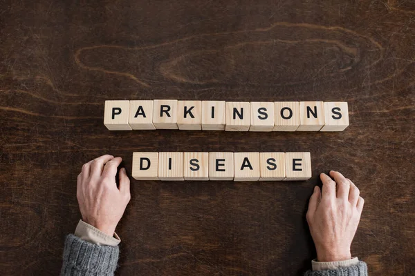 Top view of cropped senior man near cubes with parkinsons disease inscription on wooden table — Stock Photo