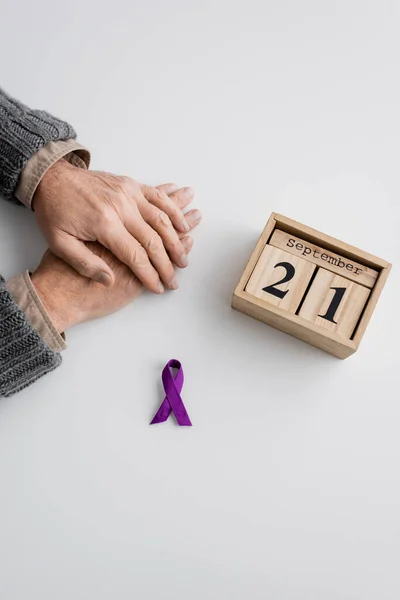 Top view of purple ribbon and wooden calendar with september 21 date near cropped man with alzheimer syndrome on white surface - foto de stock