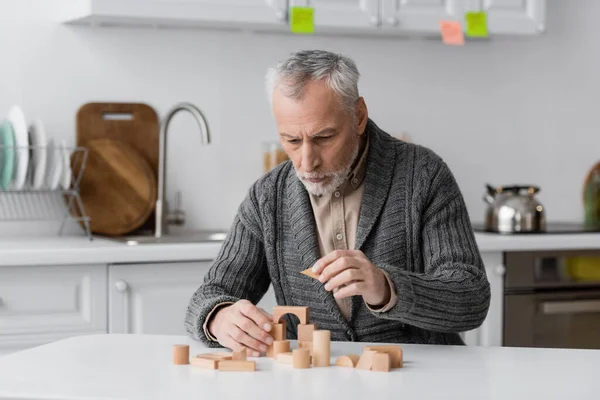Пожилой человек с синдромом Альцгеймера, играющий дома в блоки зданий — стоковое фото