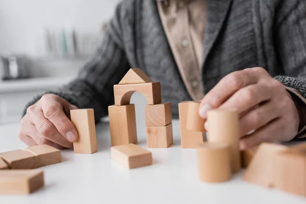 Cropped view of senior man suffering from alzheimer syndrome and playing with wooden blocks at home — Stock Photo