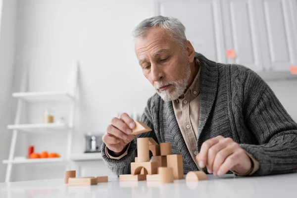 Bearded senior man suffering from alzheimer disease and playing building blocks game on table at home — Stock Photo