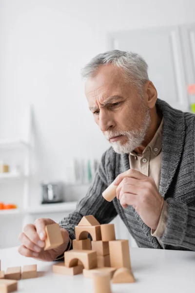 Tense man with alzheimer syndrome holding wooden block while playing therapy game at home — Stock Photo