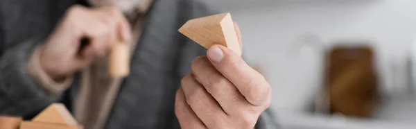 Selective focus of wooden block in hand of cropped man sick on alzheimer disease on blurred background, banner — Stockfoto