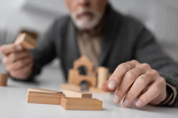 Partial view of aged man sick on alzheimer syndrome playing building blocks game on blurred background — Stock Photo