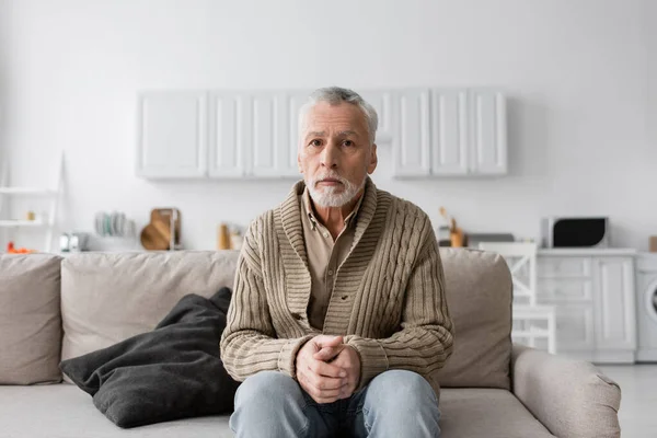 Senior grey haired man with azheimers syndrome sitting on couch at home and looking at camera - foto de stock