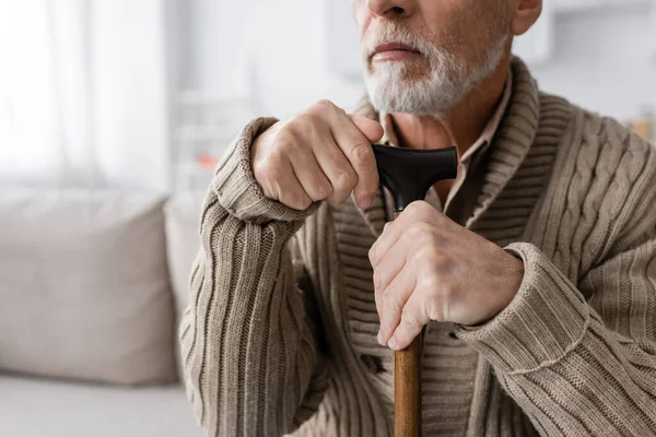 Partial view of senior bearded man with parkinson syndrome sitting with walking cane at home — Fotografia de Stock