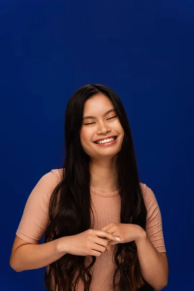 Pleased young asian woman in beige t-shirt standing isolated on blue — Stock Photo