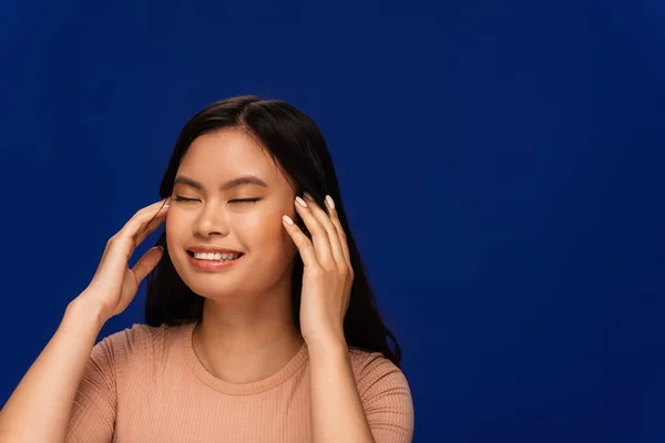 Pretty asian woman in t-shirt touching head isolated on blue — Stock Photo