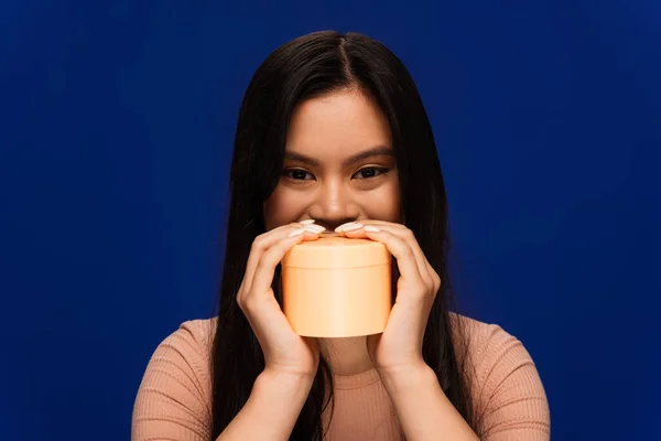 Young asian woman holding container with body cream isolated on blue — Stock Photo