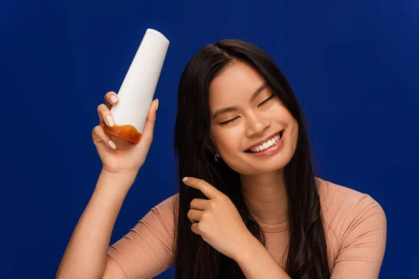 Smiling asian woman holding hair conditioner isolated on blue — Photo de stock