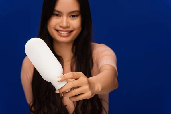 Blurred asian woman showing cosmetic lotion isolated on blue — Stock Photo