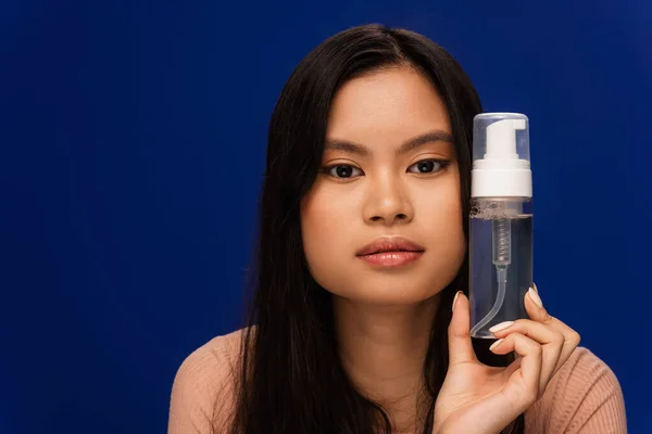 Portrait of asian woman with perfect skin holding face foam isolated on blue — Stock Photo