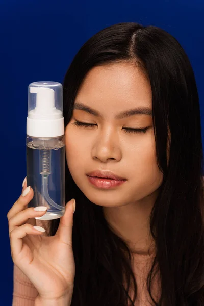 Pretty asian model with perfect skin holding face foam isolated on blue — Stockfoto