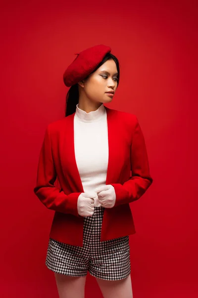 Fashionable asian model in beret and jacket posing isolated on red — Foto stock