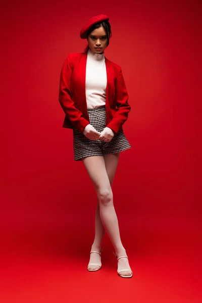 Повна довжина модної азіатської моделі в колготках і рукавичках, що стоять на червоному тлі — стокове фото