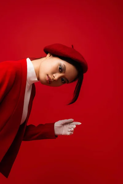 Brunette asian woman in beret and glove posing isolated on red — Stock Photo