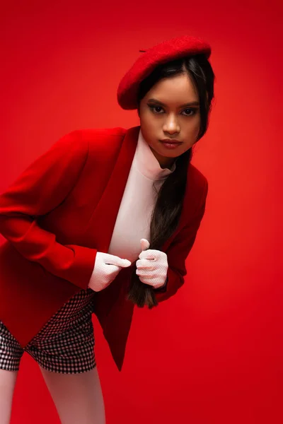 Brunette asian woman in stylish outfit looking at camera isolated on red — Stock Photo