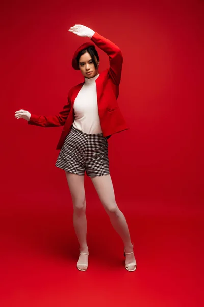 Full length of fashionable asian woman in blazer and shorts standing on red background — Foto stock