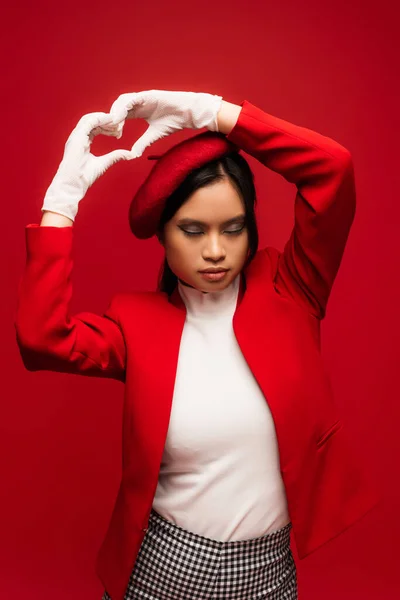Fashionable asian model in gloves showing heart sign isolated on red — Stock Photo