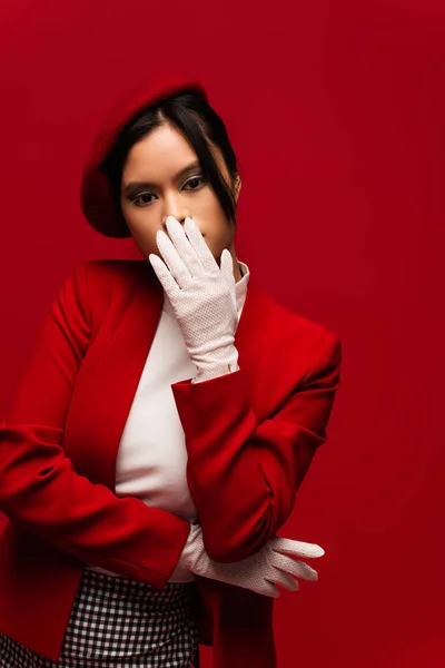 Asian woman in stylish beret and gloves covering mouth isolated on red — Photo de stock