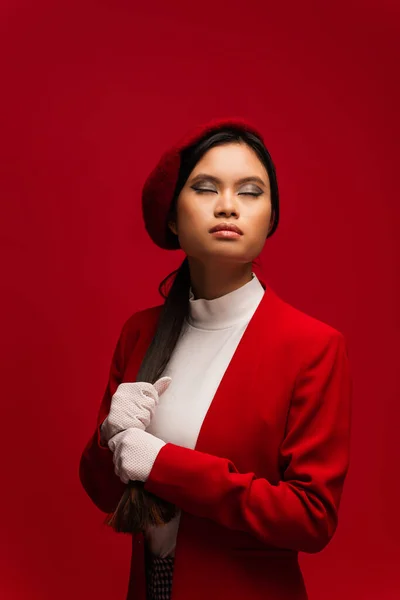 Pretty asian woman with makeup touching hair isolated on red — Fotografia de Stock