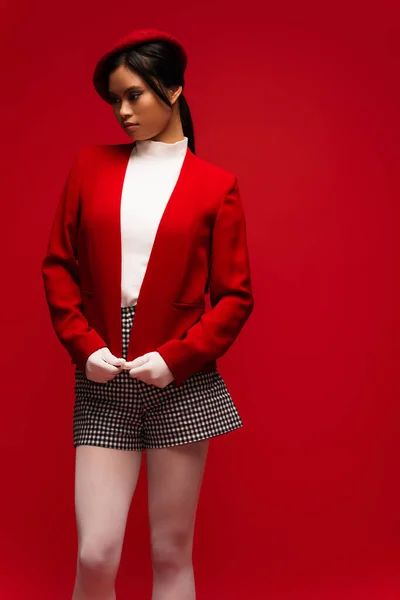 Brunette asian model in beret and gloves standing isolated on red — Stock Photo
