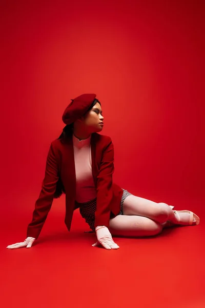 Pretty young asian model in stylish outfit sitting on red background — Photo de stock