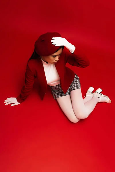 Overhead view of young asian model in stylish outfit sitting on red background — Fotografia de Stock