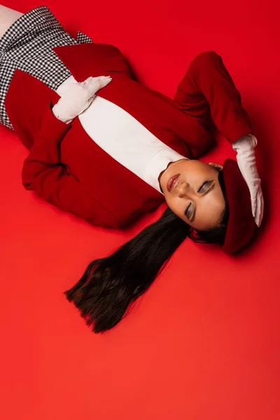 Top view of young asian model in gloves touching beret on red background — Stock Photo