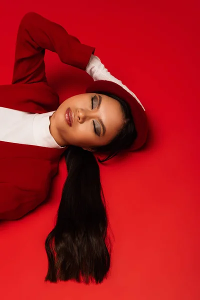 Top view of stylish asian woman in glove and beret lying on red background — Photo de stock