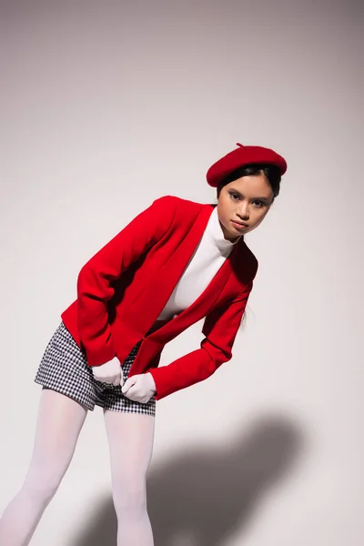 Pretty asian model in red jacket and plaid shorts posing on grey background — Stock Photo