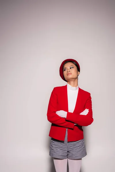 Trendy asian model in beret crossing arms on grey background — Stock Photo