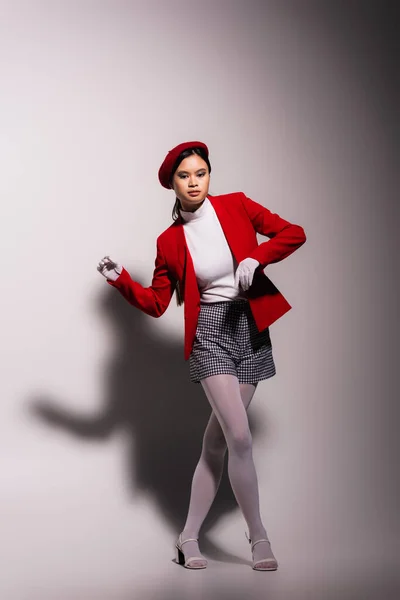 Модна азіатська модель в білих рукавичках і червоній куртці позує на сірому фоні з тіні — стокове фото