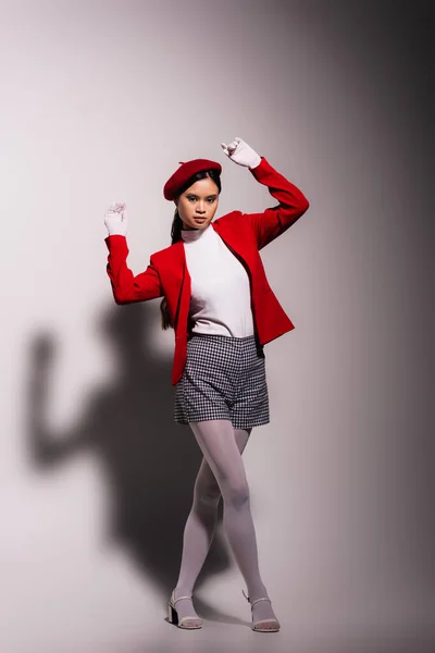 Fashionable asian model in red and white clothes looking at camera on grey background - foto de stock