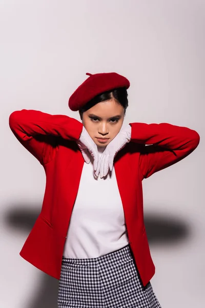 Портрет модної азіатської моделі в червоно-білому одязі, що дивиться на камеру на сірому фоні — стокове фото