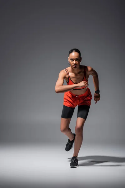 Full length of young african american sportswoman in sneakers running on grey — Fotografia de Stock