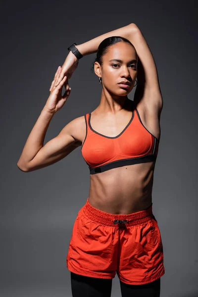 Young african american sportswoman in red sports bra posing while working out on grey — Stockfoto