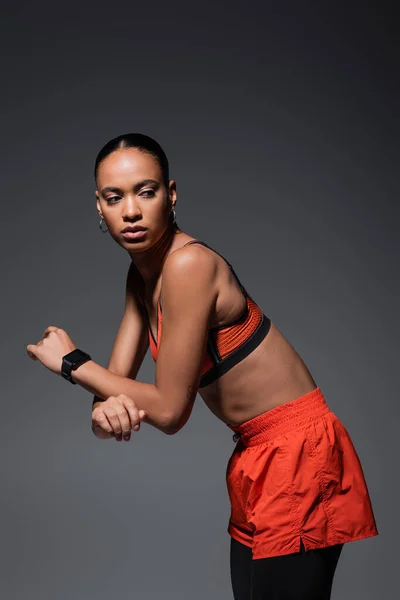 Tattooed african american sportswoman in red sports bra working out on grey — Fotografia de Stock