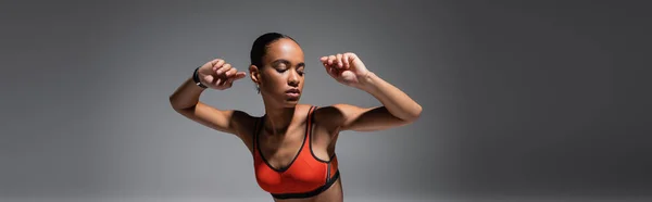 Brunette african american woman in sports bra gesturing on grey background, banner — Photo de stock