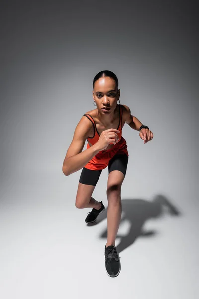 Повна довжина брюнетки афроамериканська жінка в спортивному бюстгальтері і шортах, що працюють на сірому — стокове фото