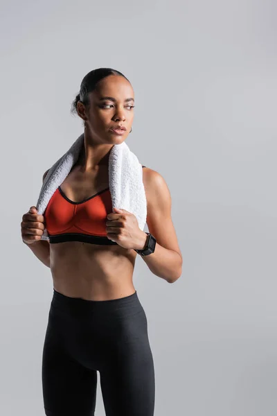 Brunette african american sportswoman in red sports bra standing with towel isolated on grey — Stock Photo