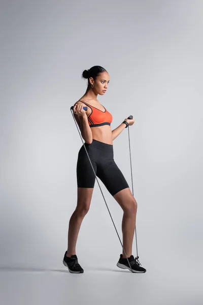 Full length of sportive african american woman exercising with jumping rope on grey — Stock Photo