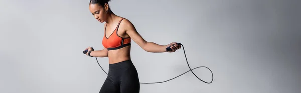 Sportive african american woman exercising with skipping rope on grey background, banner - foto de stock