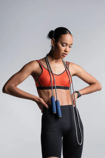 African american sportswoman standing with hands on hips with skipping rope isolated on grey — Stockfoto