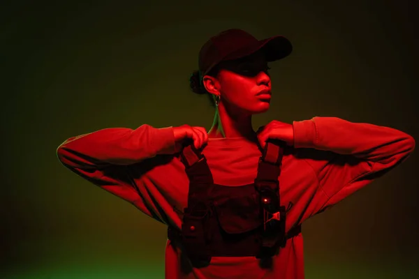 African american woman in sweatshirt and vest posing on green with red light — Stockfoto