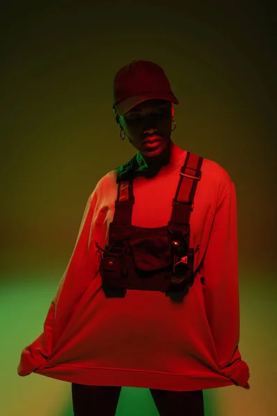 African american woman in sweatshirt and vest standing on green with red light — Stockfoto